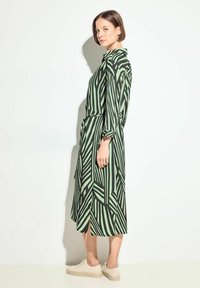Abito camicia a righe verdi e verde chiaro con maniche lunghe, vita con cintura e spacco laterale, abbinato a sneakers beige.