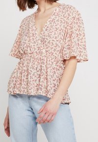 Kukkakuosi paita syvällä V-päällä, lyhyillä puffihihnoilla, kootulla vyötäröllä, vaaleanpunaisesta kankaasta, jossa on herkkiä kukkakuviota. Yhdistetty vaaleisiin farkkuihin.