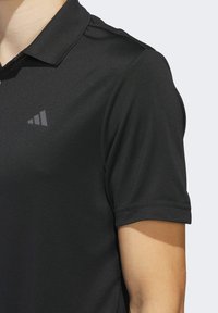 Mustapaita, joka on valmistettu sileästä kankaasta, jossa on ribbauskaulus ja lyhyet hihat, ja vasemmassa rinnassa on heijastava logo.
