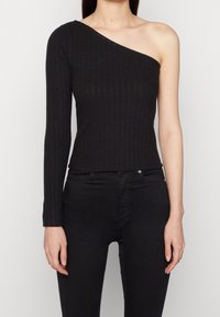 Top negro de canalé con una manga caída, que presenta un diseño ajustado y un acabado texturizado, combinado con jeans negros ajustados.