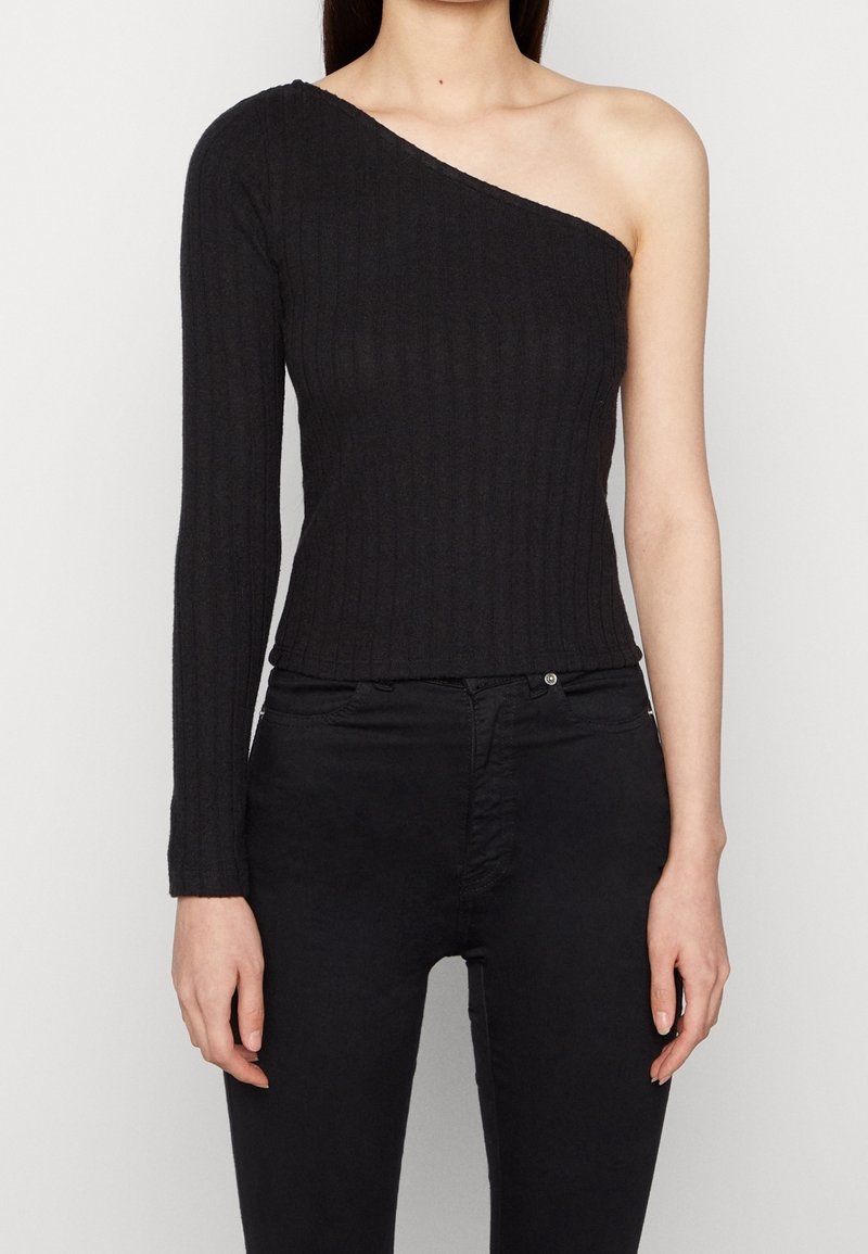 Top negro de canalé con una manga caída, que presenta un diseño ajustado y un acabado texturizado, combinado con jeans negros ajustados.