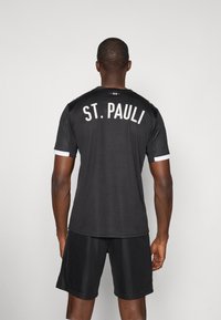 Maillot de sport noir avec "ST. PAULI" imprimé en blanc au dos. Manches courtes avec des accents blancs, accompagné de shorts noirs.