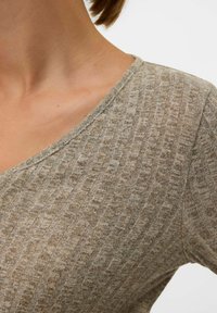 Gaiši brūns adīts tops ar V veida izgriezumu, teksturētu rakstu un īsām piedurknēm. Audums izskatās mīksts un nedaudz elastīgs.