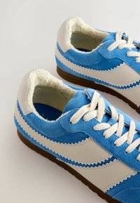 Blauwe suède sneakers met witte leren accenten, een gestructureerd ontwerp, afgeronde neus, vetersluiting en een bruine rubberen zool.
