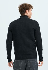 Schwarzer Strickpullover mit hohem Kragen und gerippten Bündchen. Verfügt über eine glatte Textur und eine taillierte Passform, von hinten gezeigt.