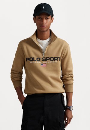 Tan zip-up sweatshirt met "POLO SPORT" en logo, met zwarte tekst en een kleine Amerikaanse vlag. Zwarte pet en shorts met zakken.