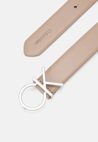 Cintura in pelle nuda con una fibbia metallica color argento "OK". La cinghia presenta un'estremità rotonda e un bordo cucito. Il marchio è impresso sulla pelle.