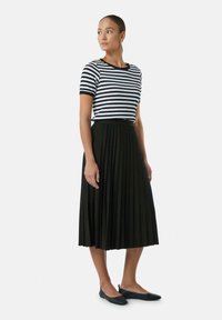 Gestreiftes Schwarz-Weiß-T-Shirt mit kurzen Ärmeln, kombiniert mit einem schwarzen, plissierten Midirock und schwarzen Ballerinas. Das Outfit hat einen runden Ausschnitt und einen elastischen Bund.