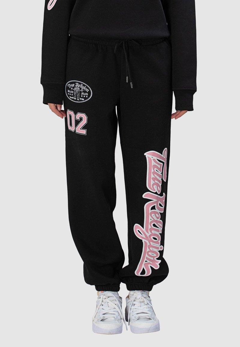 Pantalon de jogging noir avec taille à cordon, logo brodé et grands accents de texte rose. Poignets côtelés et coupe ample pour plus de confort.