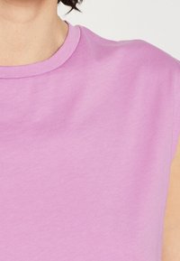 Tko s krátkým rukávem, kulatým výstřihem v měkké levandulové tkanině. Hladká textura, minimalistický design s jemnými švy kolem výstřihu.