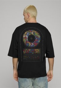 Černé oversized tričko s barevným abstraktním grafickým motivem na zádech, zobrazující kruhové a obdélníkové vzory.