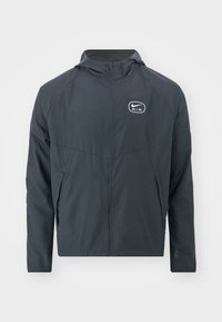 Pánská tmavě modrá větrovka z lehkého materiálu, s kapucí, zapínáním na zip a logem na hrudi. Viditelné jsou dvě boční kapsy.