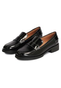 Mocassins en cuir verni noir avec un talon plat carré, présentant une couture blanche contrastante et une finition lisse et brillante.