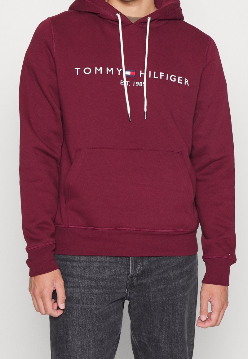 Felpa maroon realizzata in tessuto misto cotone, con una tasca frontale, cordino bianco e testo del logo sulla parte anteriore.