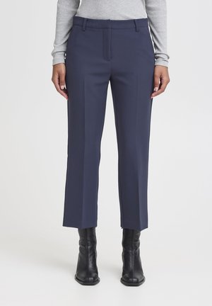 Pantaloni navy su misura con gamba dritta. Presentano pieghe frontali, tasche laterali e una texture liscia. Accoppiati con stivali neri alla caviglia.