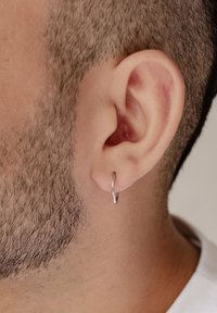 Boucle d'oreille en argent portée en gros plan, design circulaire avec une finition polie, accentuée par des cheveux courts et la texture naturelle de l'oreille.