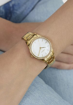 Montre-bracelet dorée avec un cadran blanc, une lunette en cristal et un bracelet à maillons dorés. Présente des index horaires simples et un cadran rond.