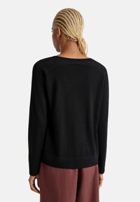 Maglione nero a maniche lunghe con scollatura a girocollo. Presenta una texture liscia e bordi a coste sui polsini e sull'orlo. Design minimalista.
