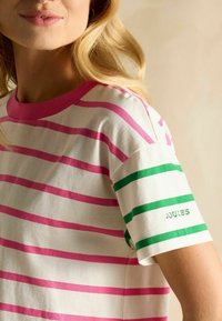 Triibuline T-särk roosa ja rohelise horisontaalsete triipudega kreemivalge tausta peal. Viimistletud roosa krae ja rohelise "JOULES" logoga varruka peal.