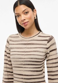 Beige og brunstripete strikkegenser med rund hals og lange ermer, med sømløs stitching og en myk tekstur.