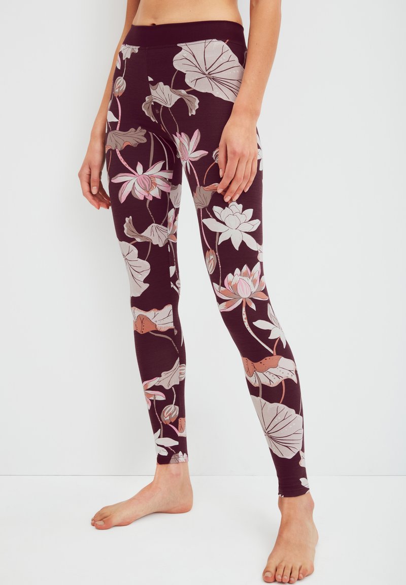 Leggings van een donker bordeaux rode stof met een bloemenpatroon van roze en witte bloemen en groene bladeren. Glad textuur, volledige lengte ontwerp.