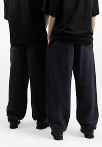 Camisetas oversize negras se combinan con pantalones de chándal sueltos de color azul marino oscuro. La tela parece suave, y los pantalones tienen bolsillos y una textura lisa.