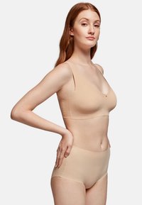 Soutien-gorge sans fil beige avec de larges bretelles, un décolleté arrondi et une couture centrale subtile. Associé à une culotte taille haute assortie. Texture lisse.