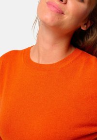 Pull en tricot orange avec un design à col rond, présentant une texture douce et une finition sans couture, mettant en avant une couleur vive.