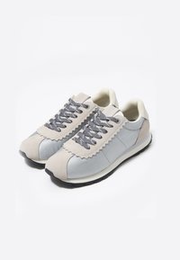 Jasnoszare sneakersy z połączeniem gładkich i teksturowanych materiałów. Posiadają ząbkowany brzeg, szare sznurówki i ciemną podeszwę.