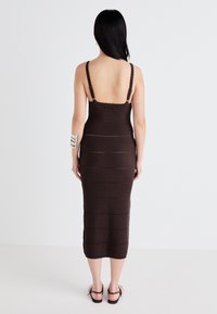 Ruda megzta midi suknelė su plonais reguliuojamais petnešomis, grioveliais ir nupjautais hemų detalėmis. Dėvima su sidabriniu apyranke.