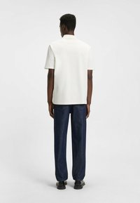 Witte korte mouwen shirt met een platte kraag, gecombineerd met een donkerblauwe rechte jeans. Eenvoudig ontwerp, gladde textuur en minimale details.