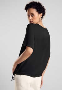 Schwarzes Kurzarmoberteil mit lockerer Passform, rundem Ausschnitt und verstellbarem Kordelzug am Saum. Glattes Material, minimalistisches Design.