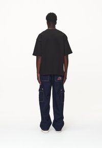 Černé oversized tričko s krátkým rukávem, spárované s tmavými džínovými cargo kalhotami s několika kapsami a kontrastním šitím.