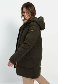 Olivengrøn, polstret parka jakke med hætte, lynlås lukning og sidelommer. Har et logo patch og tan detaljer på kraven.