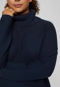 Maglione a collo alto lavorato a maglia di un blu navy, con motivo testurizzato, maniche lunghe e vestibilità rilassata. Il materiale ha un aspetto morbido e confortevole.