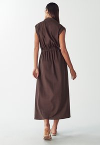 Hnedé maxi šaty s krátkymi rukávmi, golierom a elastickým pásom. Hladká látka s jemným leskom, splývajúce do lemu pri členkoch.
