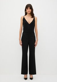 Zwarte cami met een diepe V-hals en kantdetails, gecombineerd met hoge taille, wijdvallende zwarte broeken en spitse zwarte hakken.