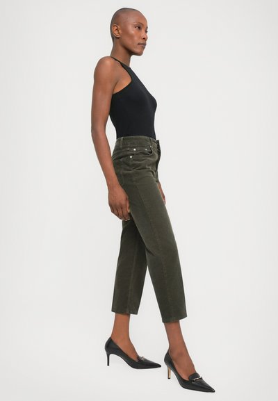 Black sleeveless bodysuit, olive green high-waisted trousers with front pockets, and black pointed-toe heels with a gold accent.