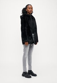 Sort faux fur hættefrakke med lange ærmer, iført over en sort ribbet top, parret med grå skinny jeans og sorte chunky hæl støvler.