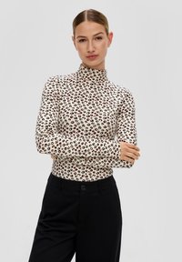 Kremowy golf w panterkę z czarnymi i czerwonymi akcentami. Długie rękawy, dopasowany krój, gładki materiał. W połączeniu z czarnymi spodniami.