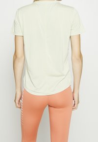 Jasnozielona koszulka z krótkim rękawem i okrągłym dekoltem; miękka w dotyku. Połączona z brzoskwiniowymi legginsami z pionowymi paskami po bokach.