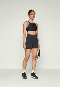Brassière de sport noire avec des accents blancs et un short noir taille haute, design ajusté, texture lisse, associé à des chaussures de sport noires.