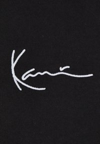 Svart tyg med vit broderad kursiv text som säger "Kani". Slät textur utan ytterligare mönster eller detaljer.