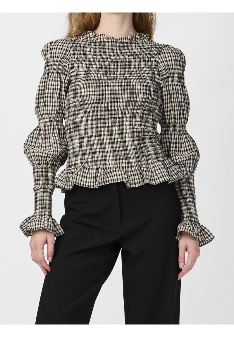 Woman wearing a black and white checkered smocked blouse with ruffled cuffs and hem, paired with black pants.