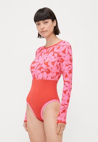 Rot- und rosa Langarm-Badeanzug mit floralem Muster im oberen Bereich und einfarbigem Unterteil; glatte Textur, figurbetonte Passform.