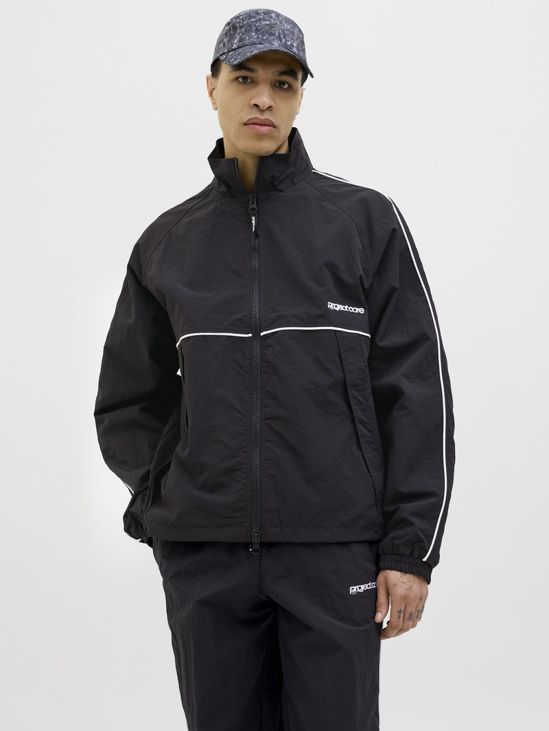 Black windbreaker jacket with white piping, high collar, and zip closure. Matched with black pants, featuring a logo and elastic cuffs.
