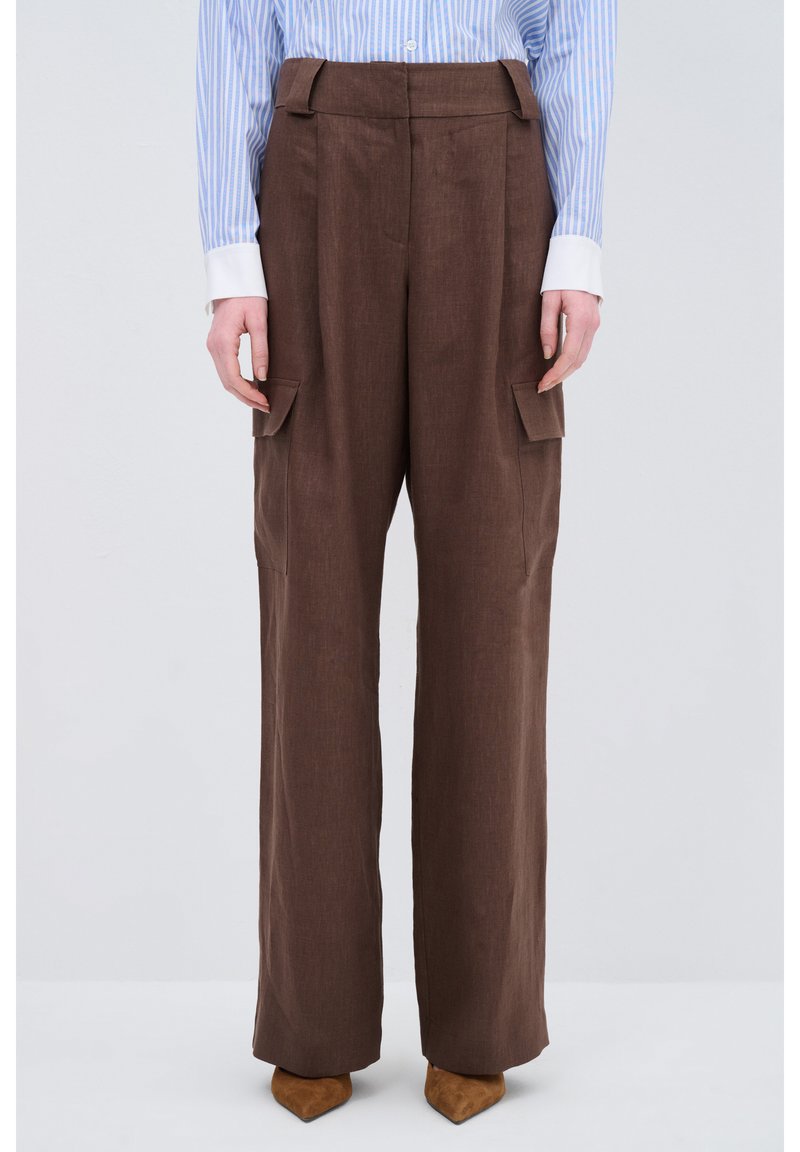 Braune, hoch taillierte Hose mit weitem Bein, ausgestattet mit Seitentaschen und einem glatten, strukturierten Stoff. Kombiniert mit spitzen, braunen Schuhen.