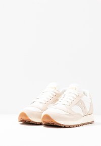 Beżowe sneakersy zamszowe i siateczkowe z białymi akcentami, z wyściełanym kostką, grubymi sznurówkami i brązową gumową podeszwą. Złote logo na języku.