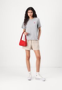 Gray T-shirt with red heart graphic, beige striped shorts, and red handbag. Model wears white high-top sneakers, showcasing casual summer attire.