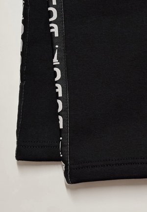 Schwarze Baumwollhose mit glatter Textur, die an der Seite einen weißen Druckakzent und sauber vernähte Säume aufweist.